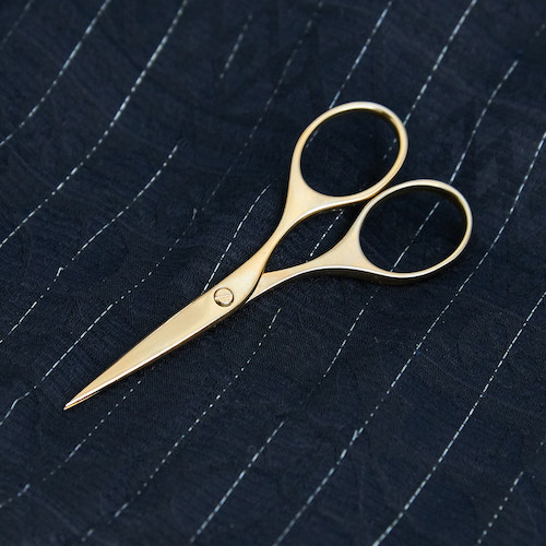 A picture of the gold plated embroidery scissor on pinstriped silk.